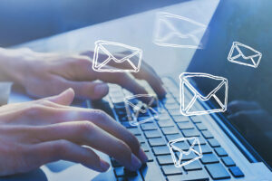 Hands type on a laptop keyboard while images of emails float through the air.