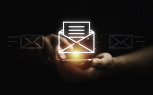 Hands use a smartphone as an open-email icon and embers of light shine above it.