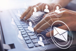 A prospecting email icon is shown being sent to several contacts, overlaid with a worker's hands typing on a laptop keyboard.
