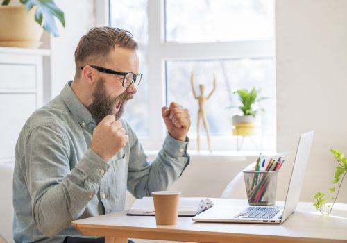 Sales Success Happy businessman feels excitement, screams, and raises his fists while looking at his laptop in a celebration of his success.