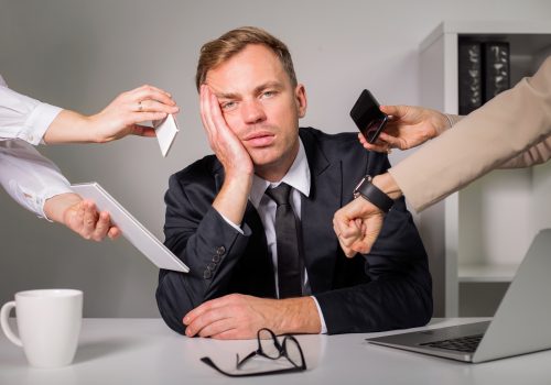 Too much busy work A tired man in a suit sits at his desk, resting his head against his hand, as four coworker hands show tasks that need his attention by holding out an envelope, phone, and watch respectively.